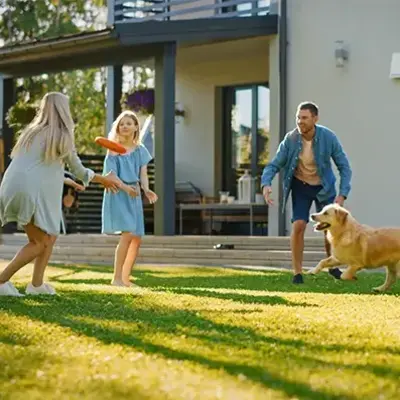 A family of four and a dog play with a frisbee on a sunny lawn. The scene exudes joy and togetherness, with a modern house in the background.