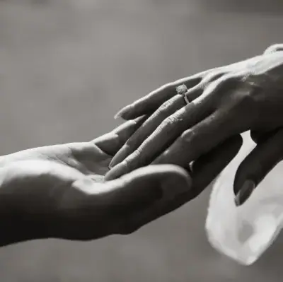 A close-up black and white photo shows two hands reaching towards each other. The hand on the right has a diamond ring, symbolizing love and connection.