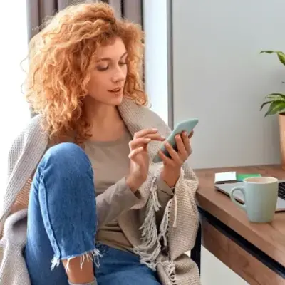 A woman seated at a desk, working on a laptop with a smartphone beside her.