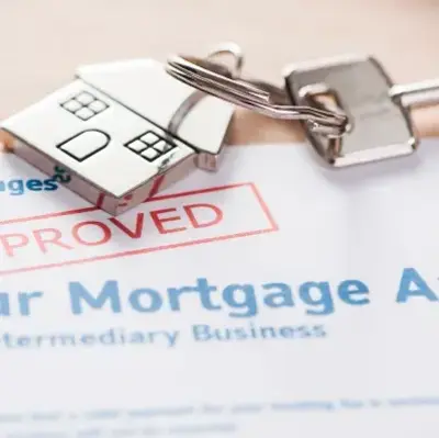 A mortgage application with "Approved" stamped in red, next to a house-shaped keychain and a key, conveying success and accomplishment in home buying.