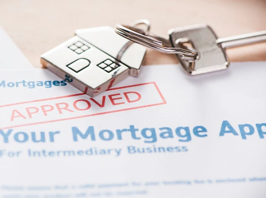 A mortgage application with "Approved" stamped in red, next to a house-shaped keychain and a key, conveying success and accomplishment in home buying.