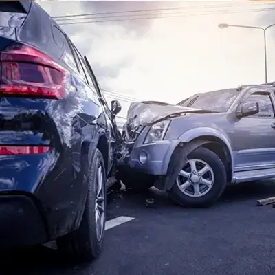 Two cars involved in a frontal collision on a road under a cloudy sky. Both vehicles show significant damage, conveying a sense of urgency.