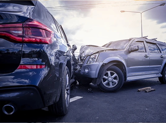 Two cars involved in a frontal collision on a road under a cloudy sky. Both vehicles show significant damage, conveying a sense of urgency.