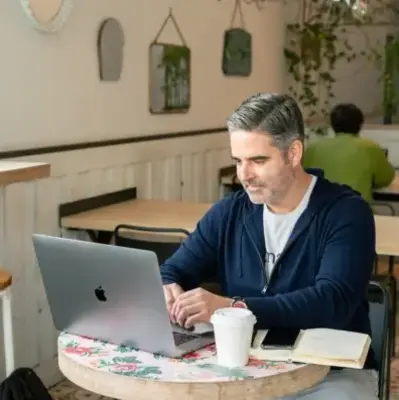 A man working on a laptop while sitting at a table, appearing engaged in his task.