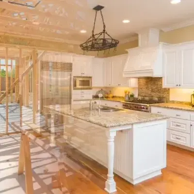 A modern kitchen with white cabinets and granite countertops is overlaid with an image of its wooden frame under construction, highlighting transformation.