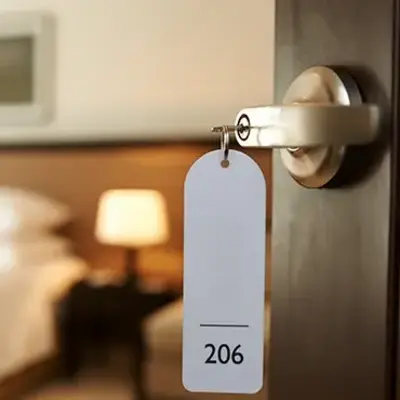 A hotel room door is slightly open, revealing a cozy interior with a neatly made bed and a warm-lit bedside lamp. A tag hangs from the door labeled "206."