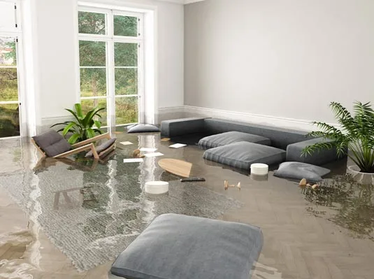 Flooded living room with submerged modern furniture, scattered cushions, and floating objects. Large windows and plants suggest a serene yet chaotic scene.