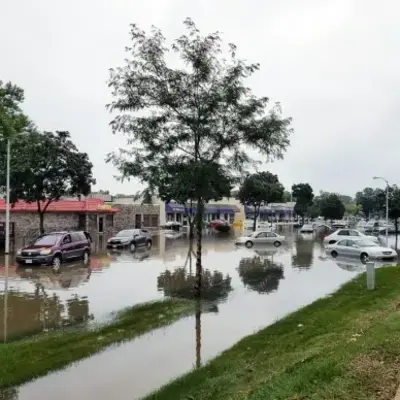 Flooded street with parked cars and a building in the background, illustrating the impact of heavy rainfall.