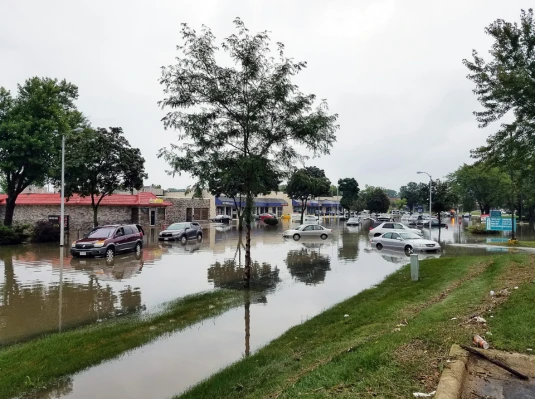 Flooded street with parked cars and a building in the background, illustrating the impact of heavy rainfall.