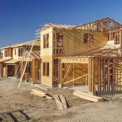 Wooden frames of houses under construction are set against a clear blue sky, conveying growth and development in a suburban area.