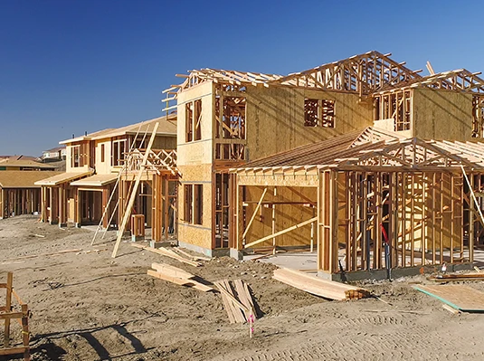 Wooden frames of houses under construction are set against a clear blue sky, conveying growth and development in a suburban area.