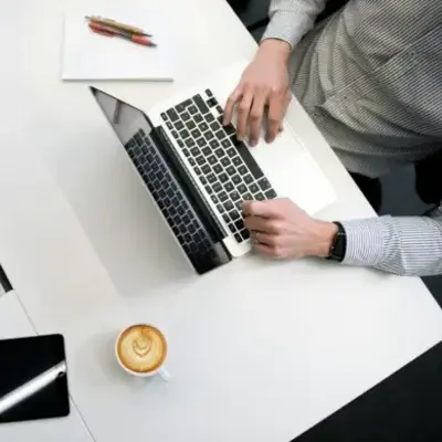 A man seated at a desk, working on a laptop with a cup of coffee beside him.