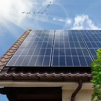 Solar panels on a tiled roof under a bright blue sky with sun rays and birds flying. Green leaves are visible in the corner, conveying sustainability.