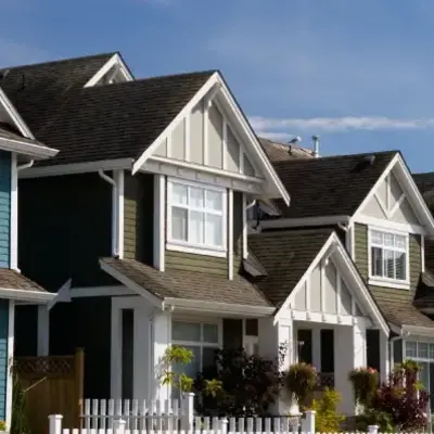 Suburban neighborhood with colorful, well-maintained houses featuring pitched roofs and white picket fences under a clear blue sky, conveying a charming, peaceful atmosphere.
