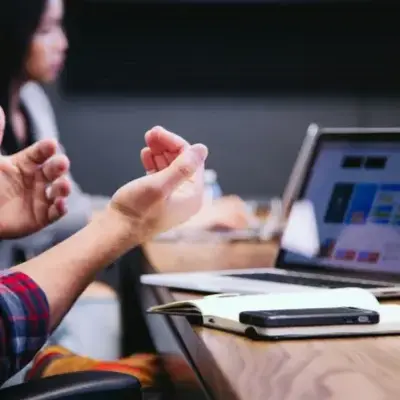 A man sits at a desk with his hands raised, appearing surprised or excited.