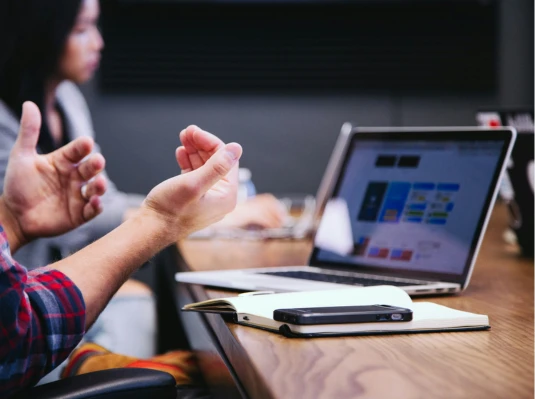 A man sits at a desk with his hands raised, appearing surprised or excited.