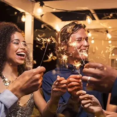 A group of people smiling and holding sparklers at a night party under string lights. The atmosphere is festive and joyful, highlighting celebration.