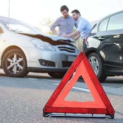 A red warning triangle is placed on the road in front of two cars that appear to have collided. Two men are inspecting the damage, looking concerned.