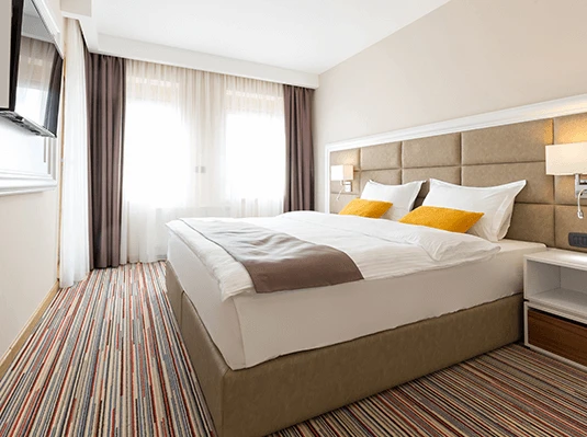 A neatly made bed in a stylish hotel room, featuring crisp white linens and decorative pillows.