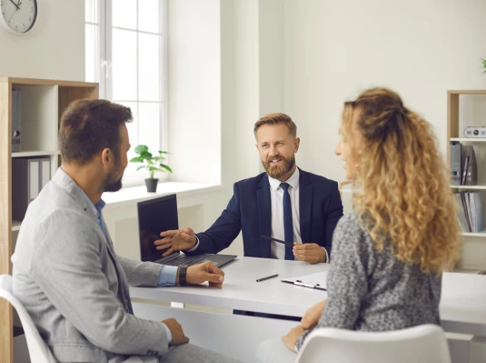 A man and woman in business attire converse with another man in a suit in a professional setting.