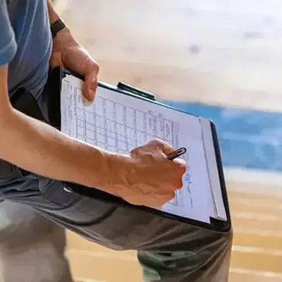 A man sits on a stairway, holding a clipboard and looking thoughtfully at his notes.