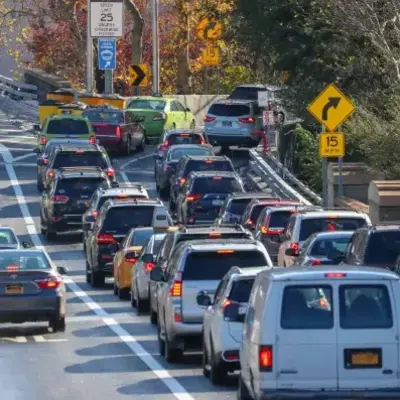 Traffic jam with numerous cars on a multi-lane road. Yellow and orange leaves indicate autumn. Signs display speed limits and caution curves.