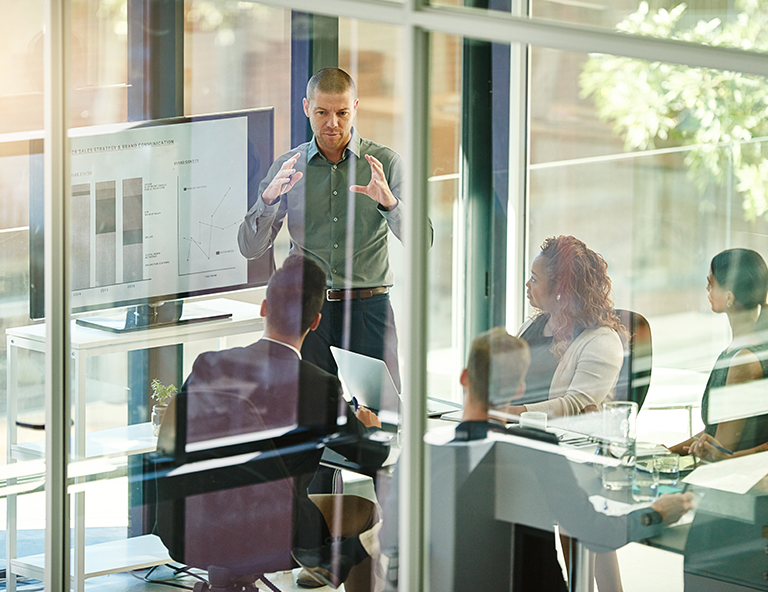 A corporate business man presenting in an open, glass encased conference room, showcasing a bright and open atmosphere.